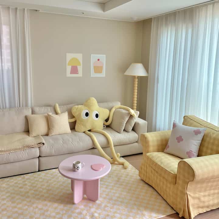 Beige and yellow toned living room featuring a beige sofa, yellow check armchair, cute star cushion, and a pink coffee table with a cozy atmosphere