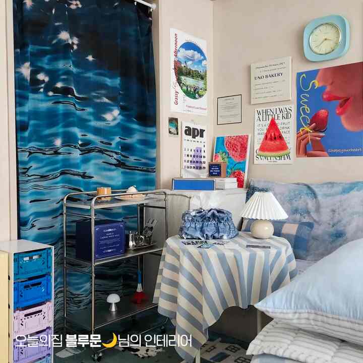 青とグレーの色調のリビングルーム、大きな青いファブリックカーテンと青いパターンのソファ、多彩な壁のアートが配置された雰囲気のある空間