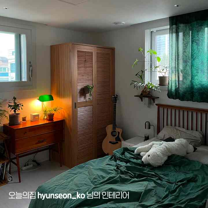 ナチュラルな木目調とグリーンカラーの調和が感じられる小さな寝室、木製家具と植物が温かみのある雰囲気を演出している