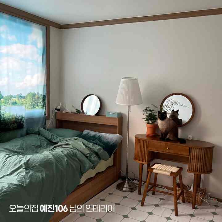 ナチュラルな木目調とグリーンが調和した寝室、ベッドと化粧台に二匹の猫がいる雰囲気のある空間