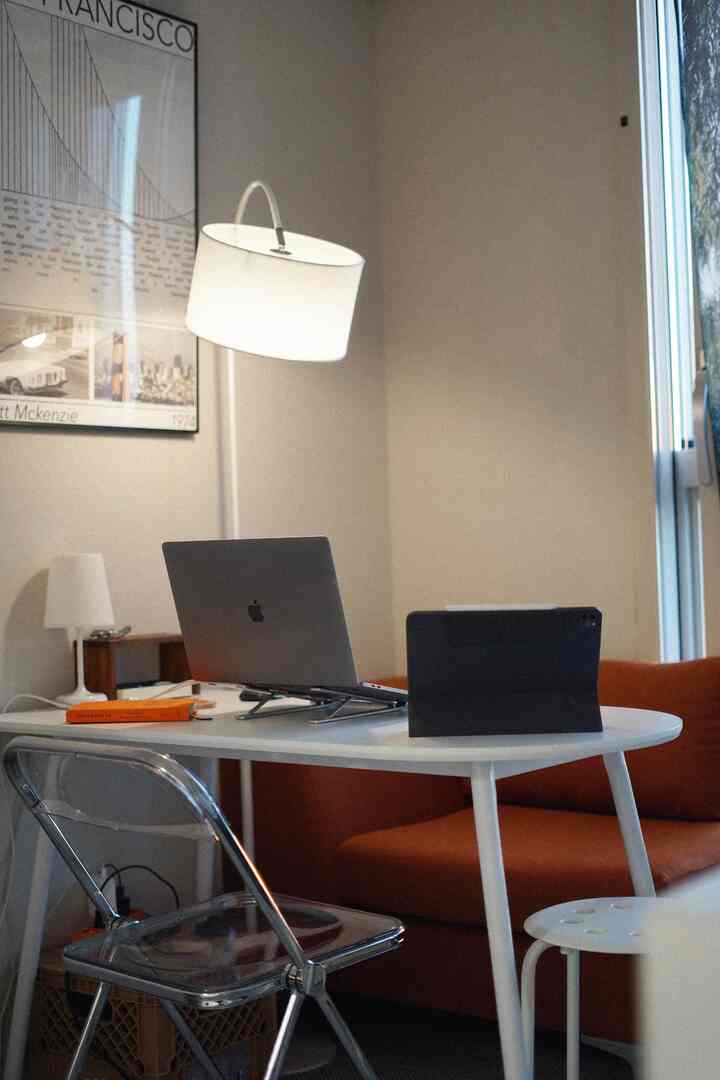 A white and orange toned studio workspace featuring a single sofa and transparent folding chair in a cozy office setup