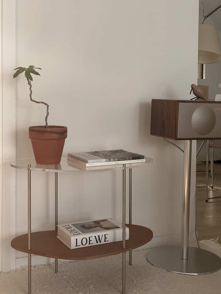 ブラウンとホワイトの色調のリビング、透明なアクリルと木製の棚に小さな植物と雑誌が置かれたミニマルなインテリア