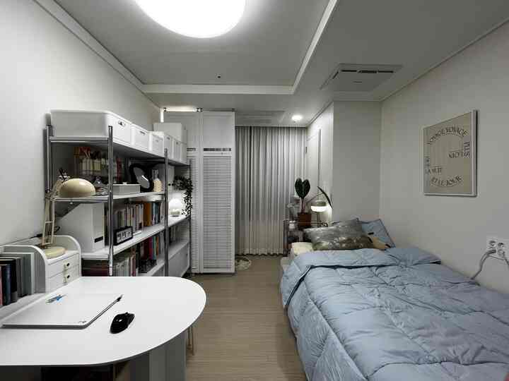 White and natural tone bedroom featuring bed, desk, and bookshelf creating a clean and practical ambiance