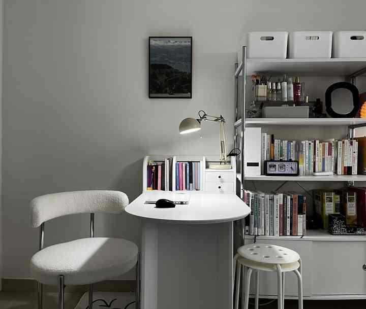 White-toned home office study featuring a desk, bookshelf, and stools with a clean, bright atmosphere
