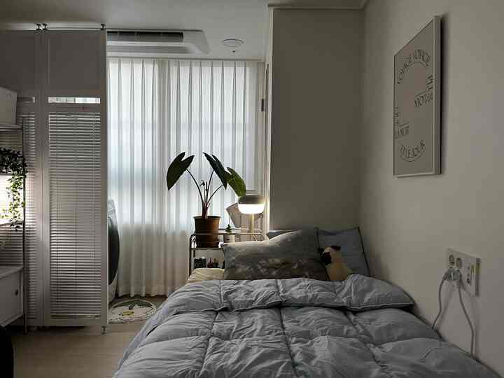 スカイブルーの寝具と白いカーテンが配された寝室、すっきりとした広々としたレイアウトが特徴の落ち着いた空間