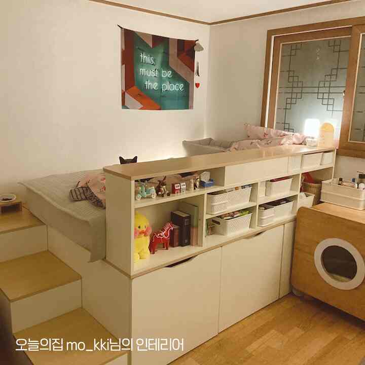 ベージュとホワイトの色調の小さな寝室、階段型収納が配置され、猫がいる雰囲気のあるインテリア