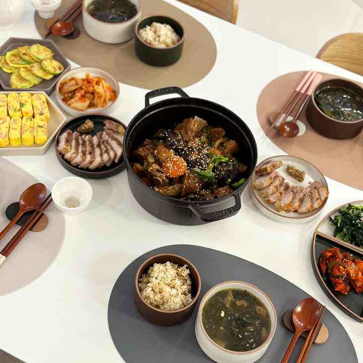 White and beige toned dining room featuring a table set with braised pork ribs and assorted Korean side dishes