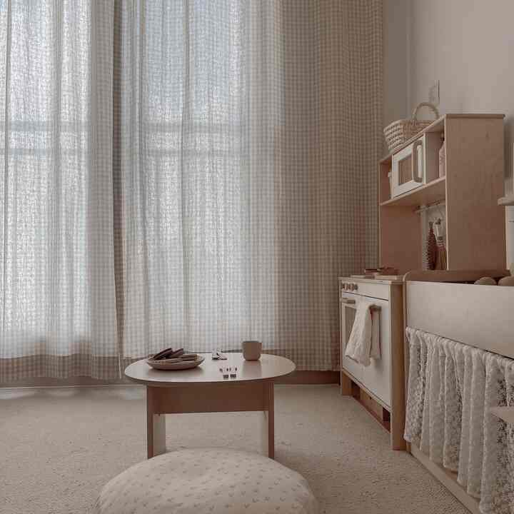 柔らかなベージュと木目調が調和した子供部屋、チェックのカーテンとベビー向け家具が配置された自然な雰囲気の空間