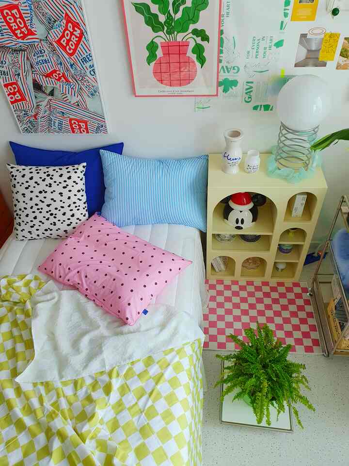 A bedroom with white walls and modern posters, featuring a checkered duvet and colorful pillows on the bed, creating a cozy atmosphere