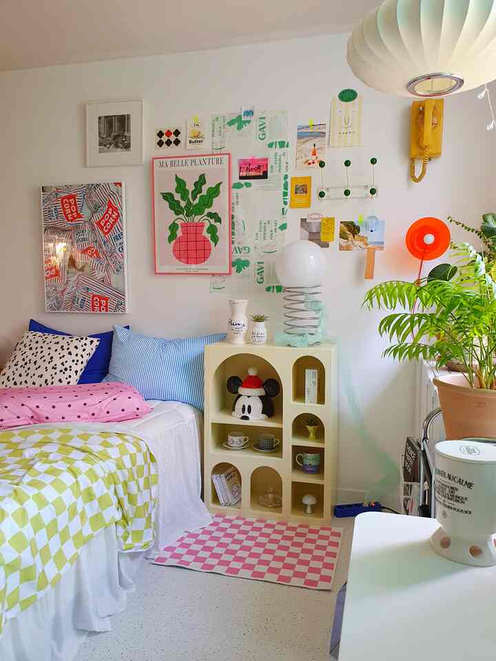 パステル調のコンパクトな寝室、レトロな黄色の電話や壁飾り、クッションと個性的なスパイラルフロアランプが配置された温かみのある空間