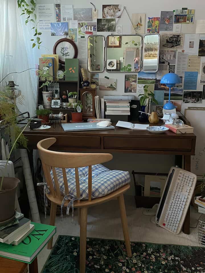 Cozy study and home office with warm brown wood tones and green plants, featuring vintage tri-fold mirror and various decorative items