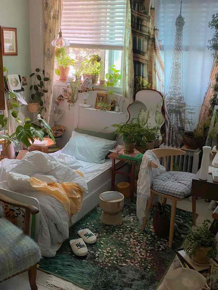Natural-toned studio bedroom in white and green featuring a flower-patterned rug and abundant plants creating a cozy atmosphere