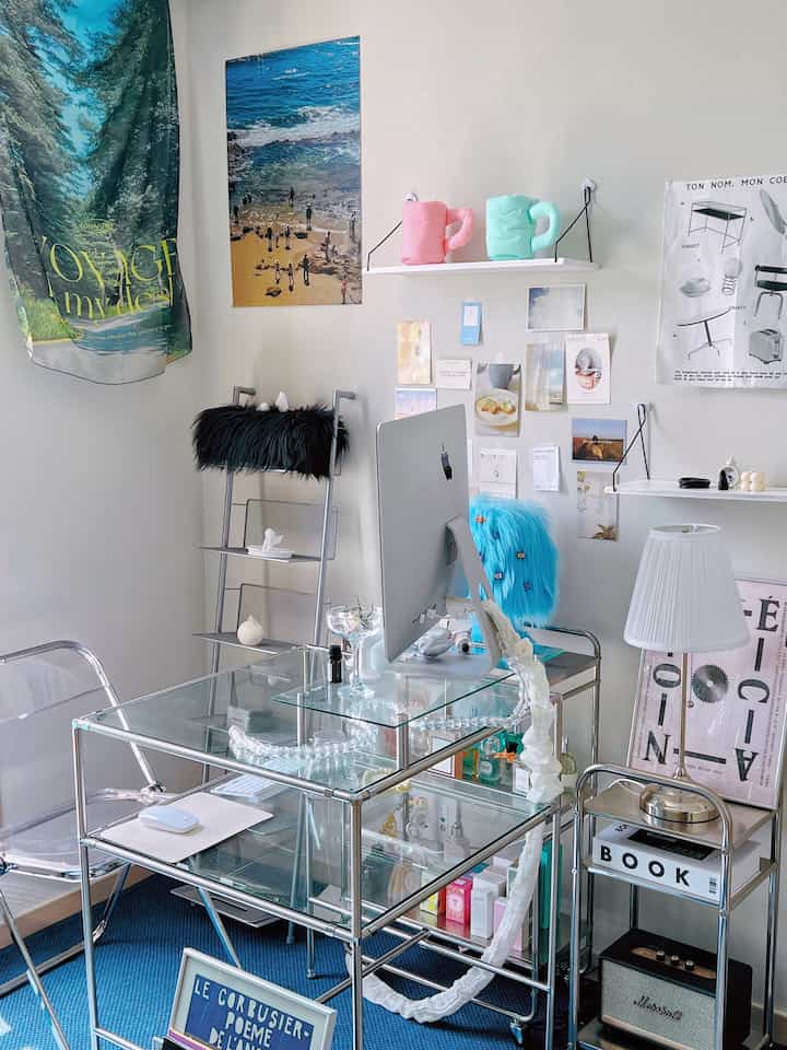 透明アクリルチェアとガラスデスクが配置されたミッドセンチュリーモダンの書斎、ポスターや棚が配された印象的な空間