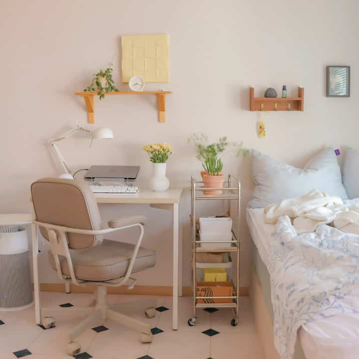 明るいホワイトトーンのワンルーム寝室とホームオフィス、机の上に黄色い花と植物が置かれた温かみのある雰囲気のあるインテリア