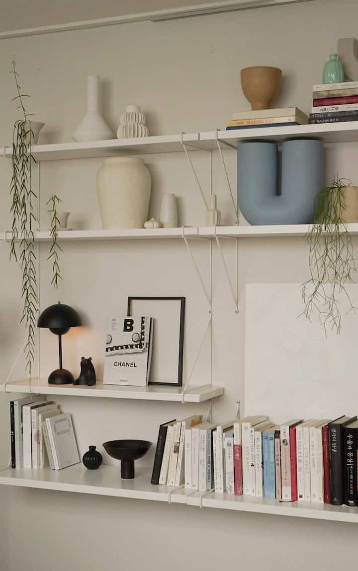 Minimal natural interior space with white walls and shelves featuring ceramic objets, books, and plants