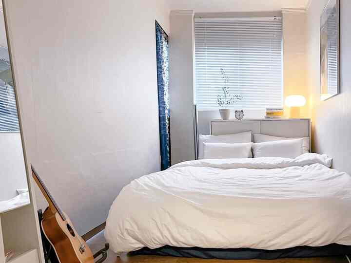 Bright white-toned bedroom featuring a double mattress bed, corner storage with full-length mirror, creating a clean and airy space