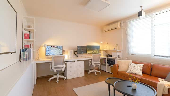 White and brown toned home office workspace featuring neatly arranged desks, office chairs, and a leather sofa creating a comfortable atmosphere