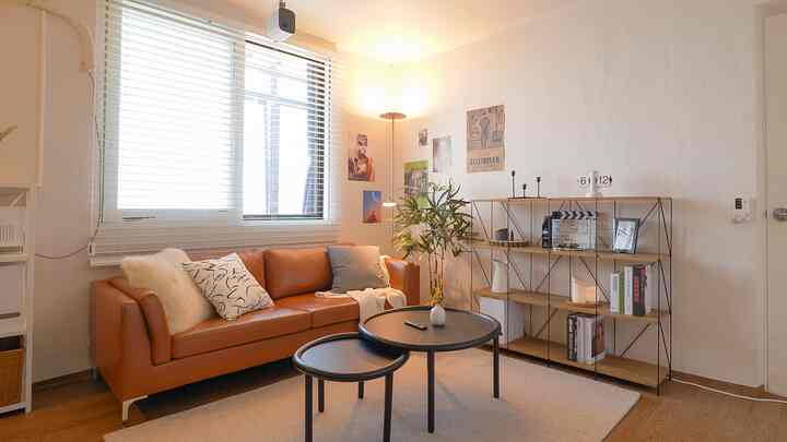 温かみのあるナチュラルカラーのリビング、キャラメル色の3人掛けソファと丸いコーヒーテーブル、木製棚とラグが配置された居心地の良い空間