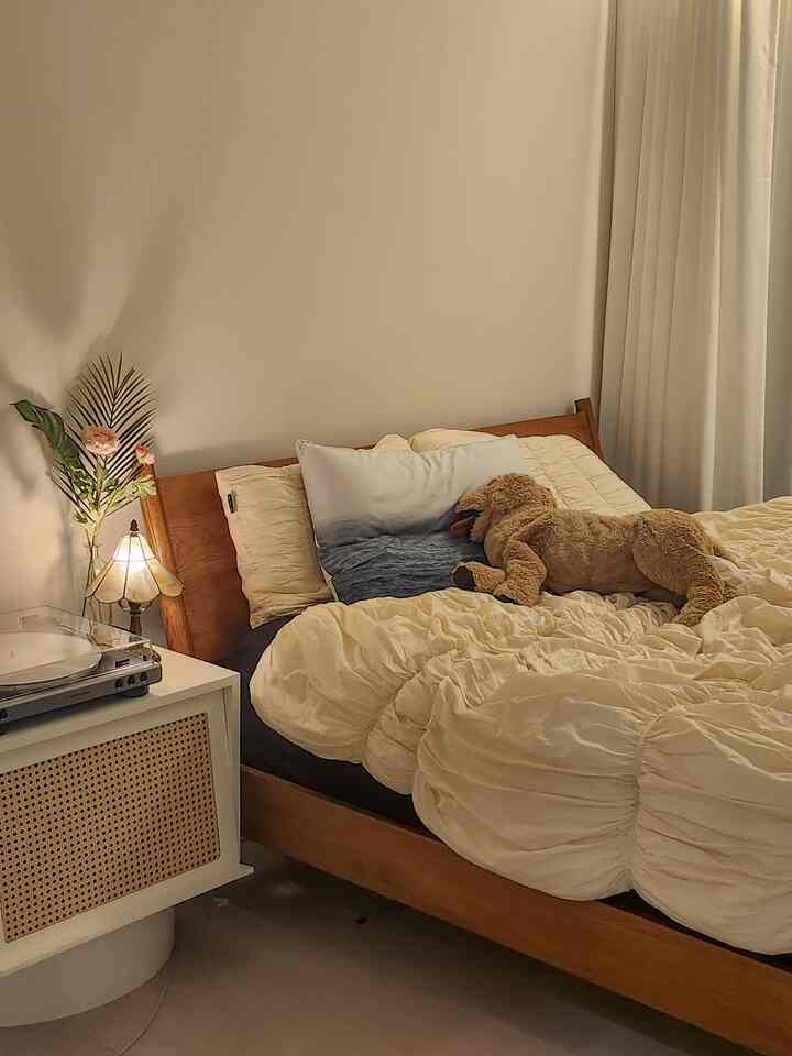 暖かいベージュと木目調の落ち着いた寝室、イケアのぬいぐるみ犬と居心地の良い寝具が配置されたシンプルなインテリア