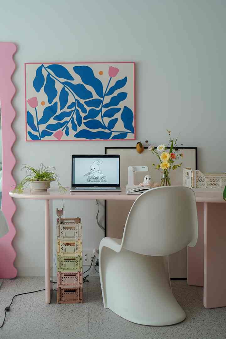 パステルピンクのホームオフィス、ピンクのデスクにノートパソコンと植物、カラフルなポスターが調和したシンプルで雰囲気のあるインテリア