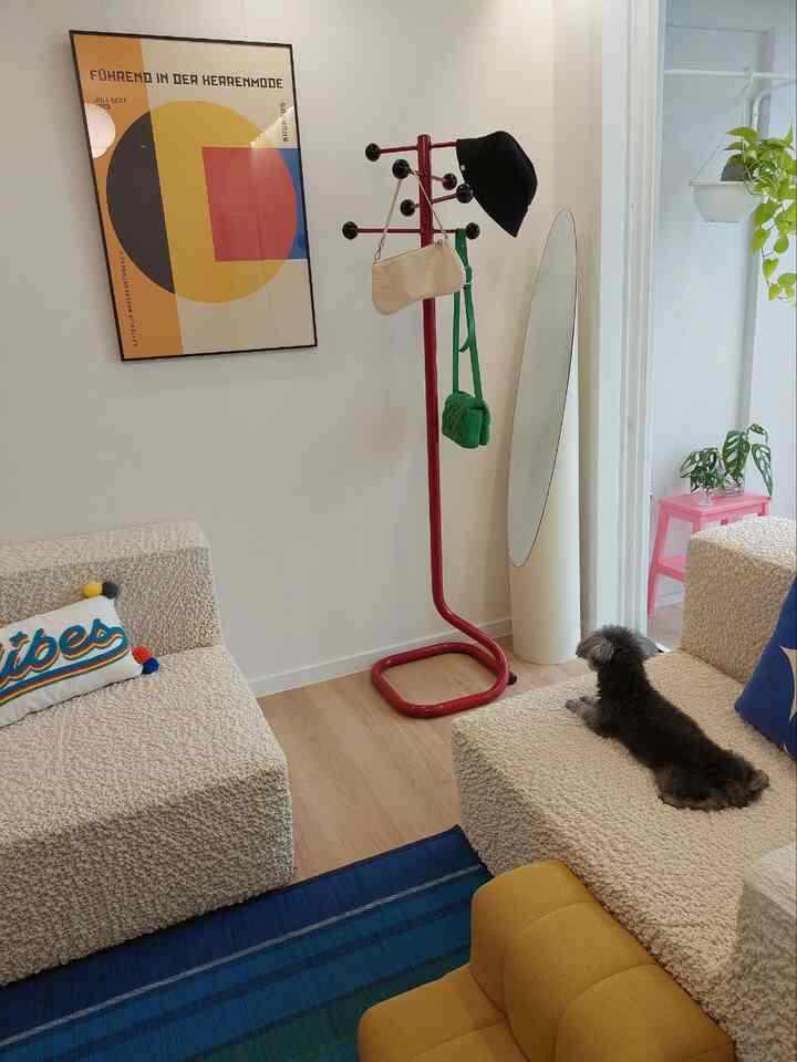 Beige-toned living room featuring two sofas, a central red coat rack, and a small dog, creating a cozy atmosphere
