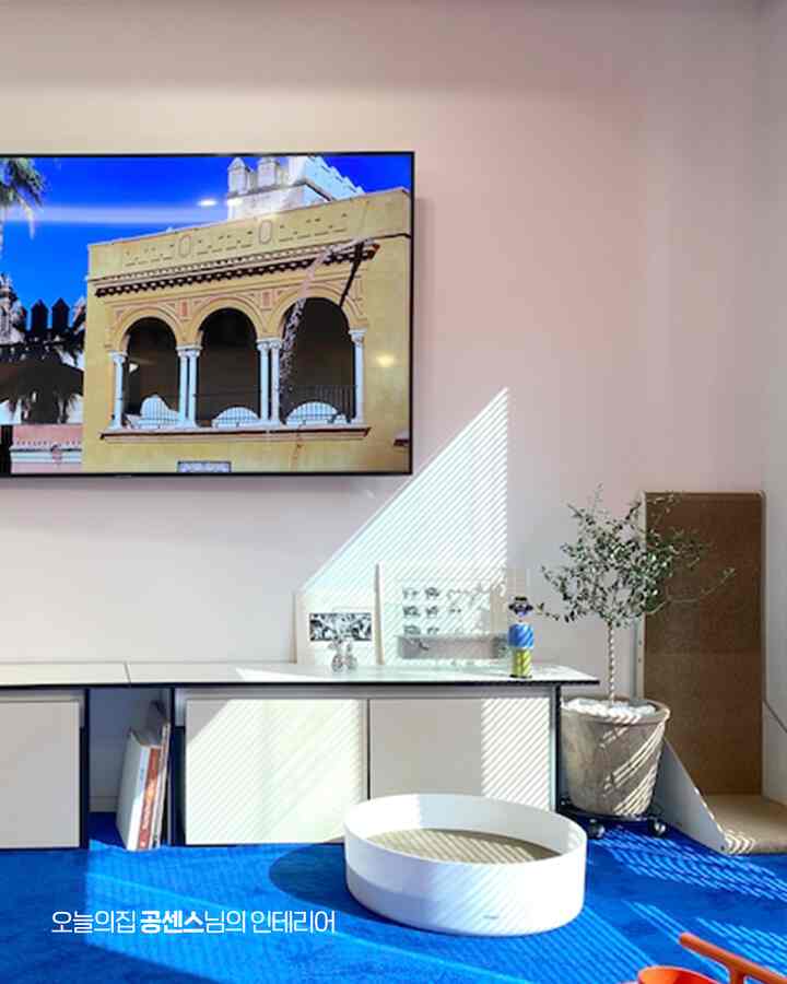 明るいホワイトとブルーのトーンのリビング、猫用の爪とぎとテレビ台が配置された居心地の良い空間