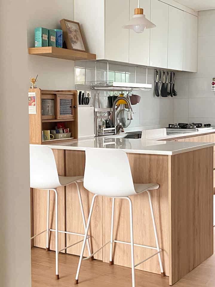 A natural wood tone and white kitchen featuring a kitchen island and pendant light with a clean, serene atmosphere