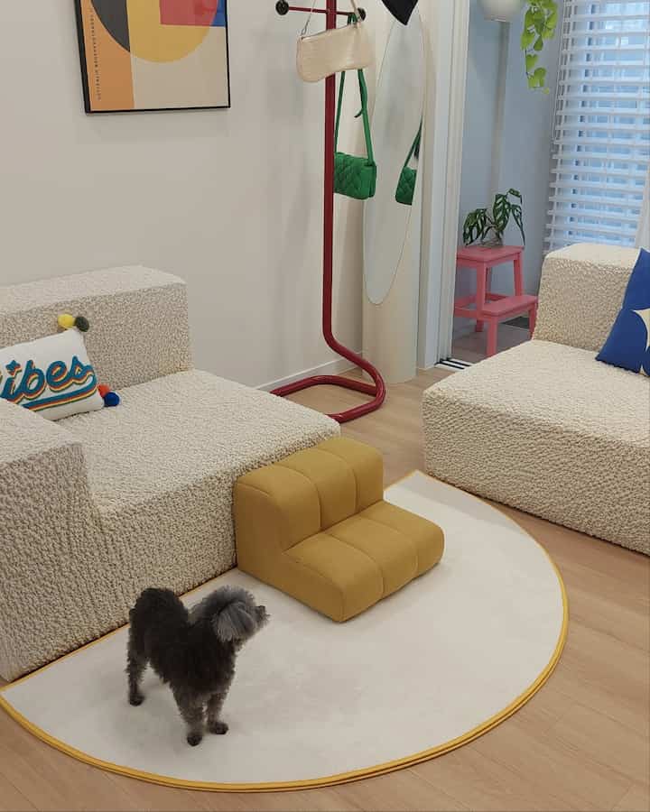 Natural wood tone living room featuring beige sofas, yellow pet steps, and a small dog creating a cozy atmosphere