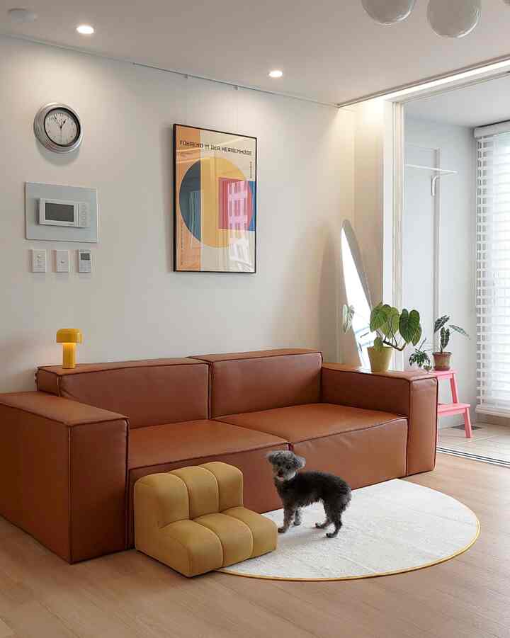 明るいミッドセンチュリーモダンのリビング、茶色の木目調レザーソファと黄色のペットステップ、丸い白いラグの上に犬がいる