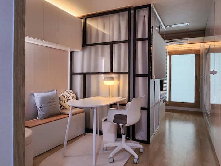 ホワイトと木目調が調和したワンルーム、透明のエンボスパネル間仕切りとデスク・椅子が配置されたモダンで清潔感のある作業スペース