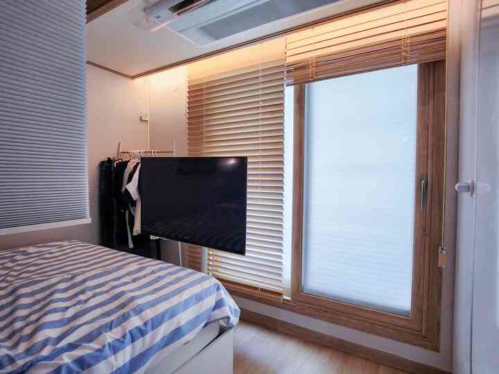 A white and wood-toned bedroom featuring a mobile TV stand and striped bedding creating a cozy atmosphere