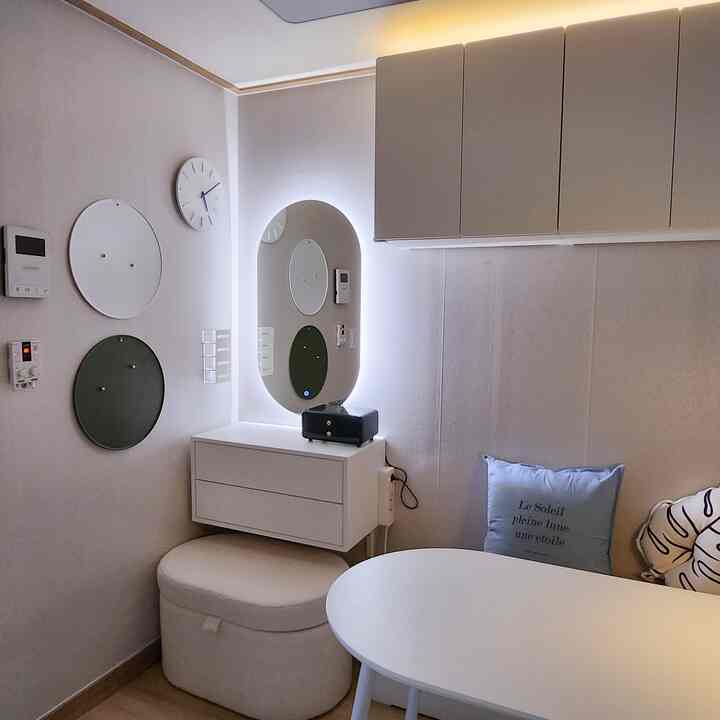 White and natural tone two-person room featuring a lighted oval mirror, vanity, storage stool, and round table in a cozy setting