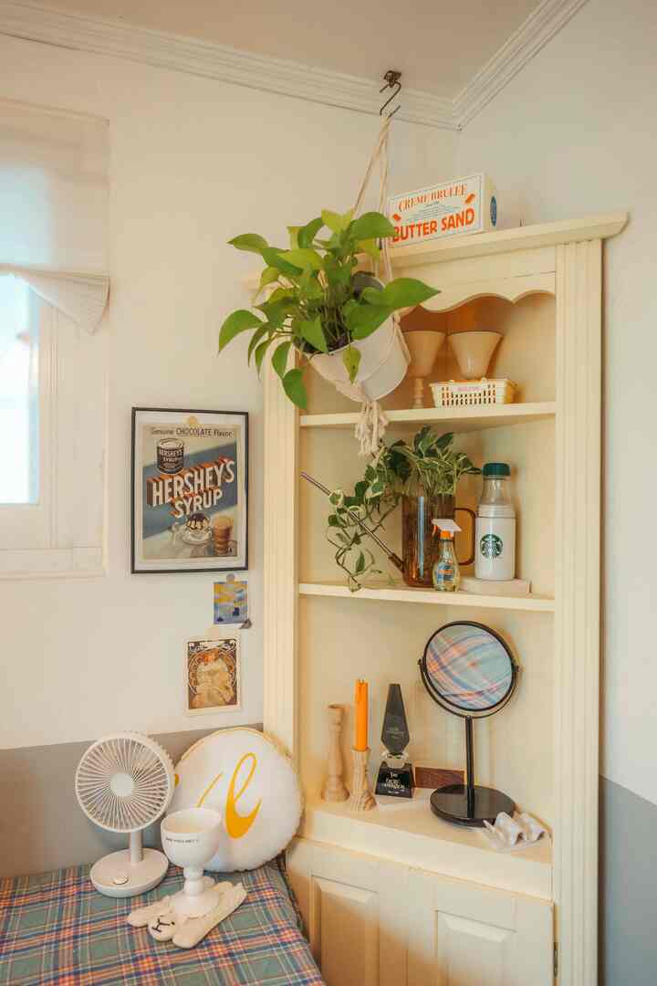 白とアイボリーの色調のリビングのコーナー収納、植物とポスターが配置された雰囲気のあるナチュラルな空間