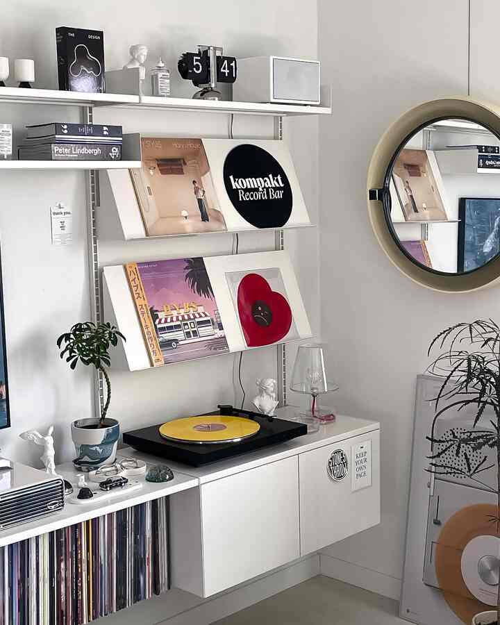 White-toned living room featuring vintage records, a turntable, shelving, and a round mirror for a modern music listening space