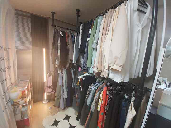 ホワイトとウッドトーンが調和するワンルームのウォークインクローゼット、L字型ハンガーラックとフロアランプ、収納付きミラーが配された印象的なインテリア