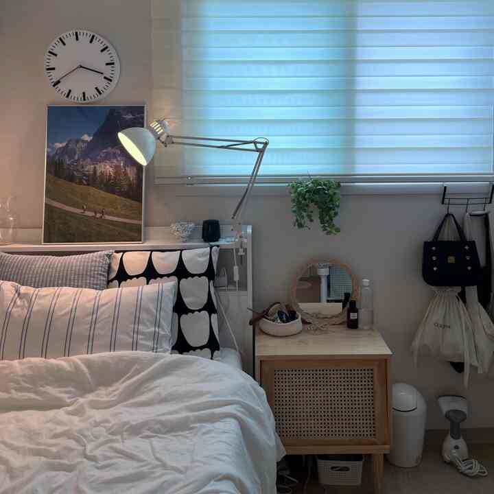 Calm white and wood-tone bedroom featuring picture frame, desk lamp, and nightstand with a natural interior atmosphere