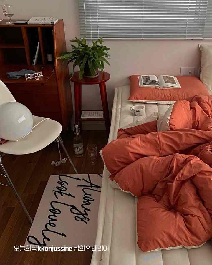 ベージュと木目調が調和した小さな寝室、オレンジ色の寝具と自然の要素が温かみのある雰囲気を演出