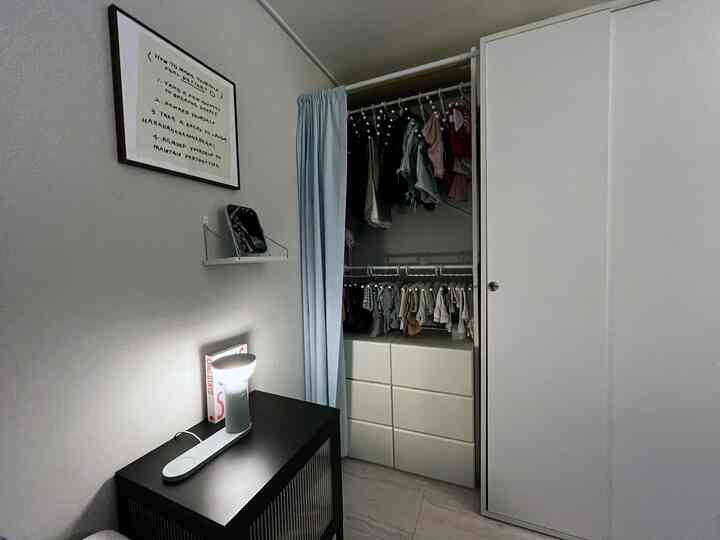 ナチュラルトーンの寝室のウォークインクローゼット、スカイブルーのカーテンで覆われたスライディングドアのワードローブとハンガー、ドレッサーが配置された落ち着いた空間