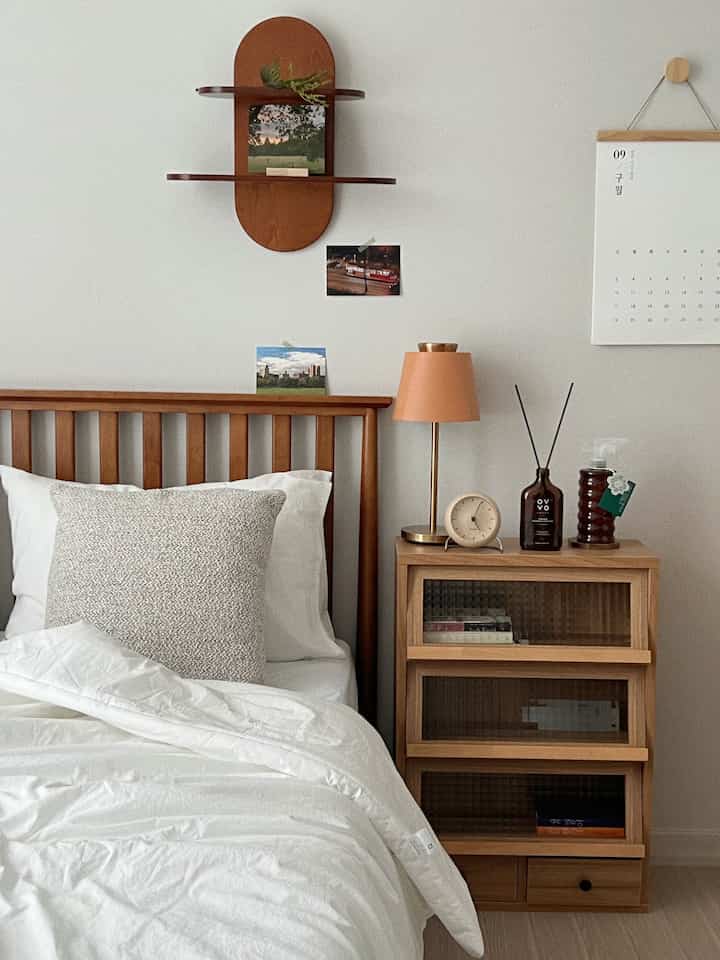 Simple bedroom with white bedding and wood tone furniture, featuring wall shelf and nightstand creating cozy atmosphere