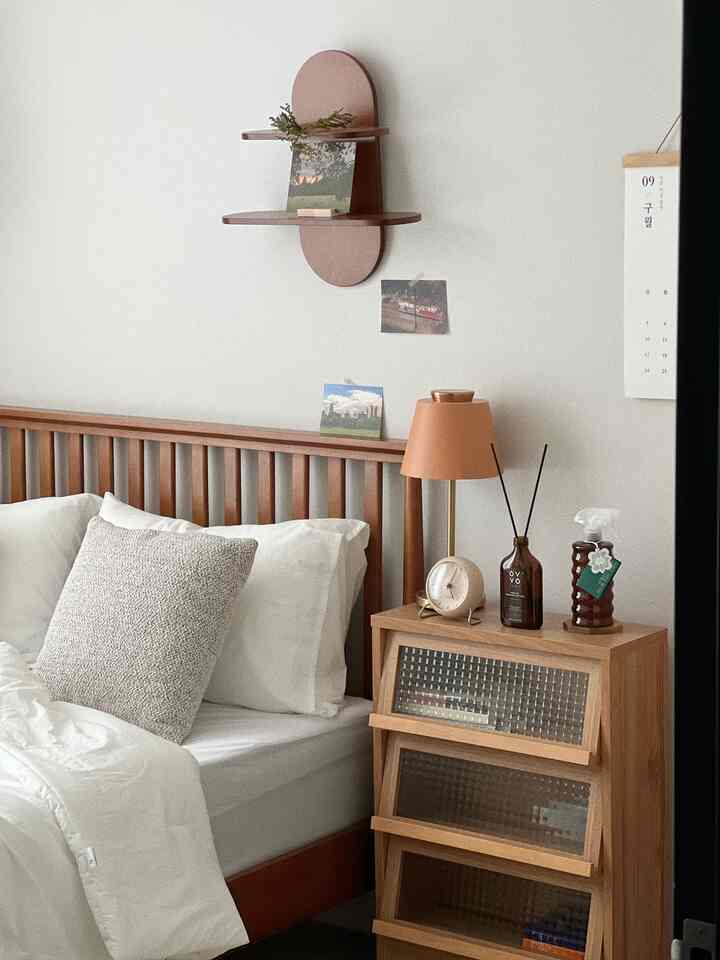 White bedding with wood tone bed frame and nightstand in a natural-feeling bedroom space