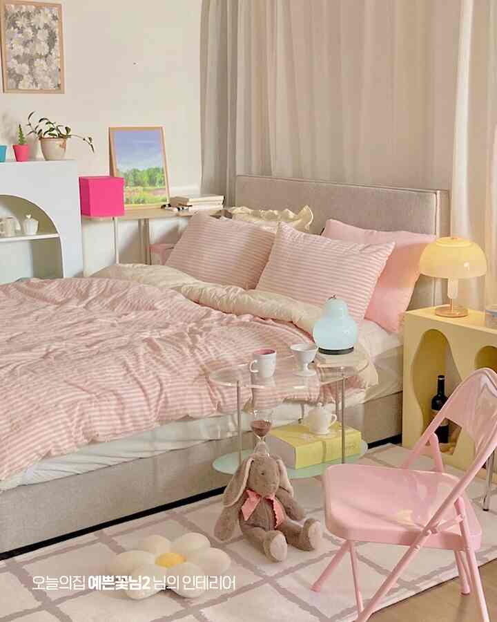 ピンクとベージュの色調の寝室、ピンクの寝具とベージュのベッドフレーム、温かみのある照明ランプが配置された雰囲気のあるインテリア