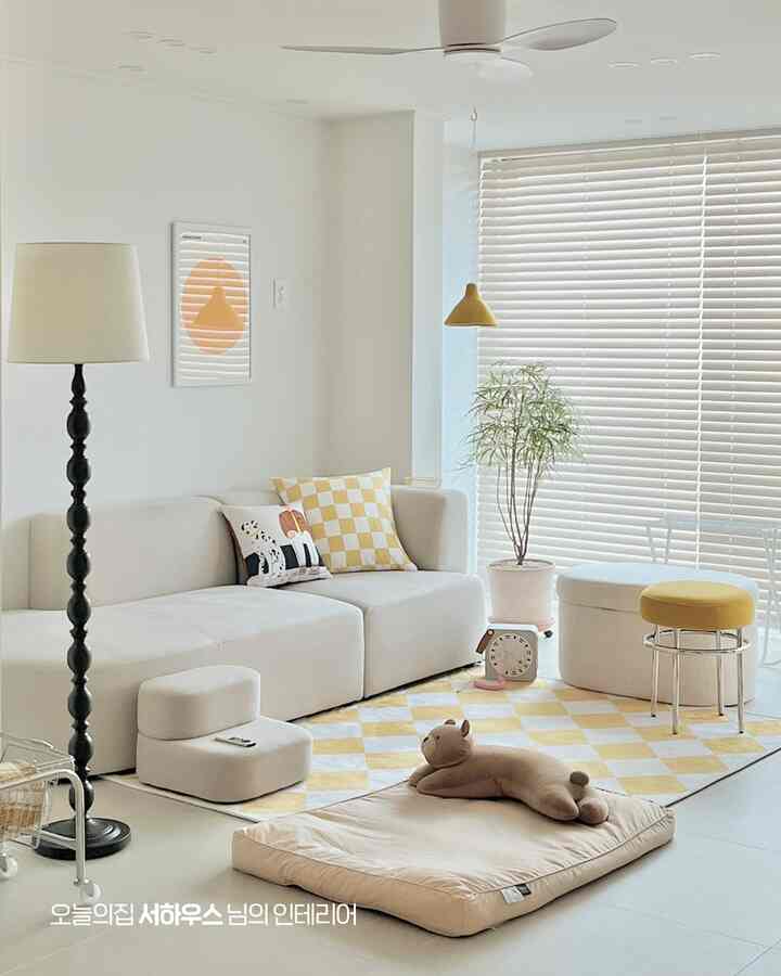 白と黄色のトーンのリビングルーム、ベージュのソファと黄色のチェック柄ラグが配置された明るく居心地の良い空間