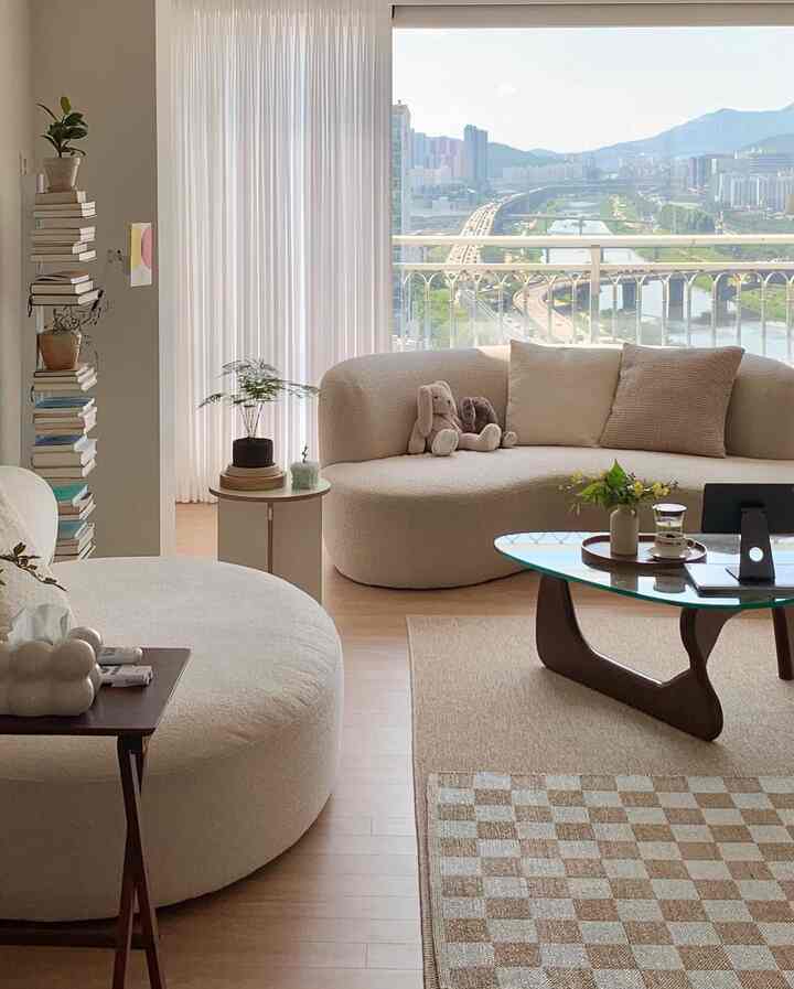 Bright white and wood tone living room featuring curved sofa, coffee table, and a scenic river view creating a cozy atmosphere