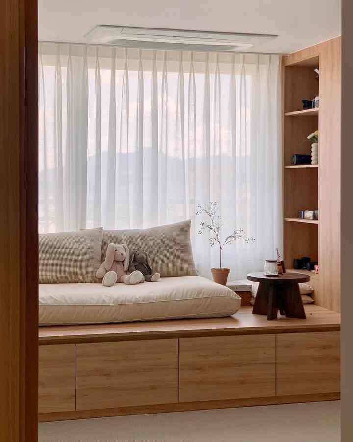 温かみのあるウッドトーンと白を基調とした平床インテリアの子供部屋兼リビングスペース、ぬいぐるみのウサギとカーテン、小さな植物が配置された雰囲気のある空間