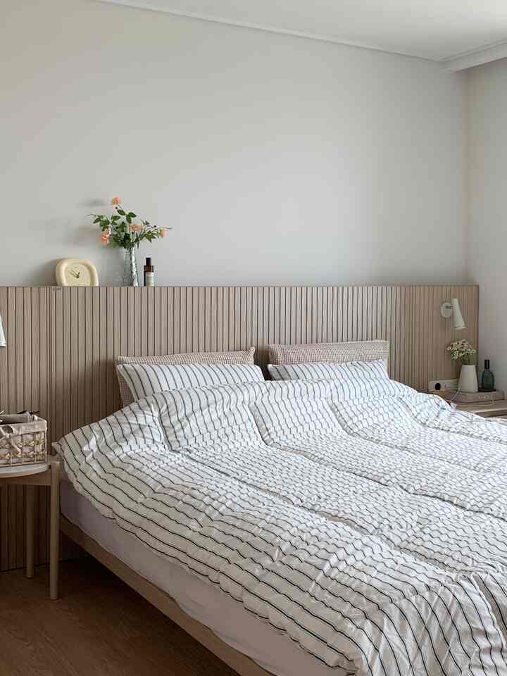 Soft white and wood-tone bedroom featuring striped bedding and large bed frame in a cozy hotel-like setting
