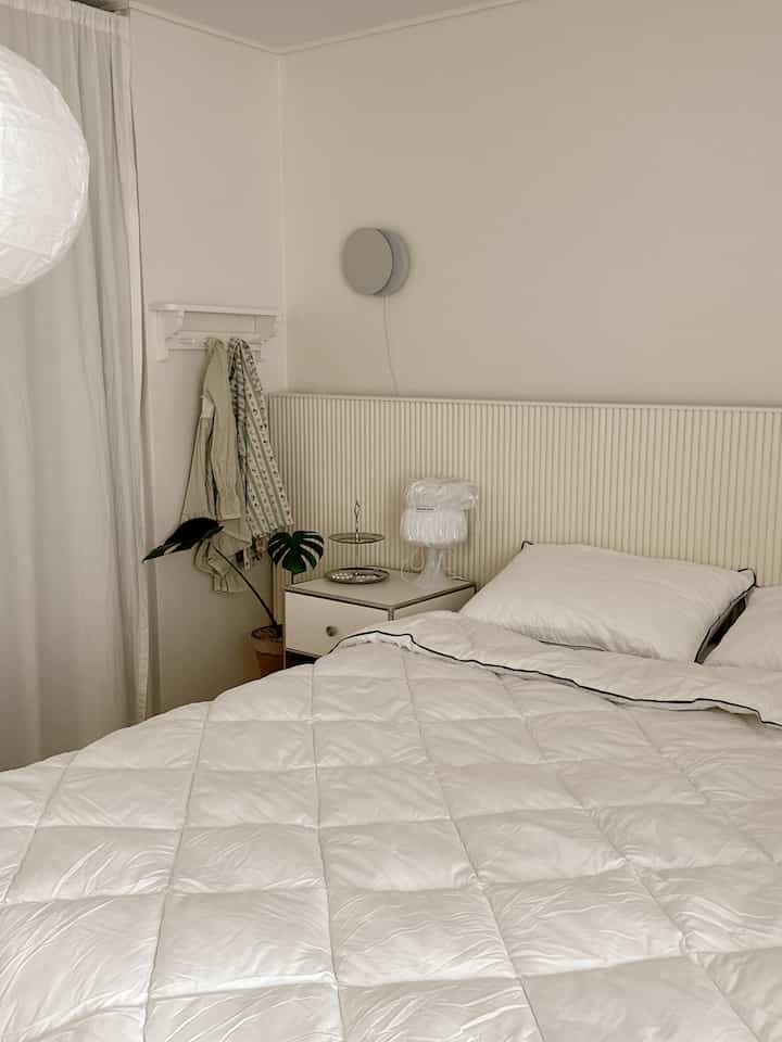 白を基調とした寝室、整った寝具とナイトテーブル、モダンな照明と植物が配されたシンプルモダンな空間