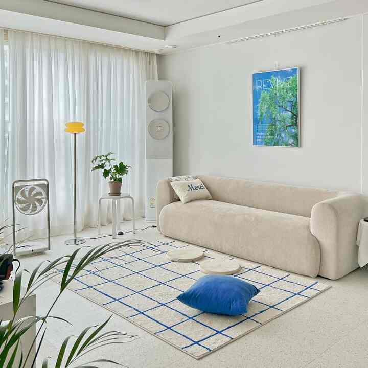 White and blue toned living room featuring beige sofa, plants, fans, and a rug in a modern, clean interior