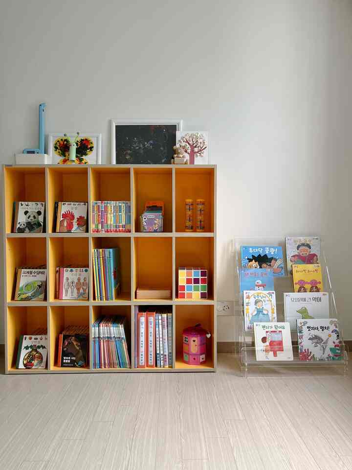Bright white-walled children's space featuring an orange bookshelf and organized children's books and toys in a clean Nordic style interior