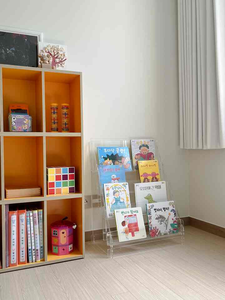 ナチュラルカラーとオレンジ色が調和した子供部屋、透明なアクリル本棚とオレンジ色の棚が配置された明るく清潔感のある空間