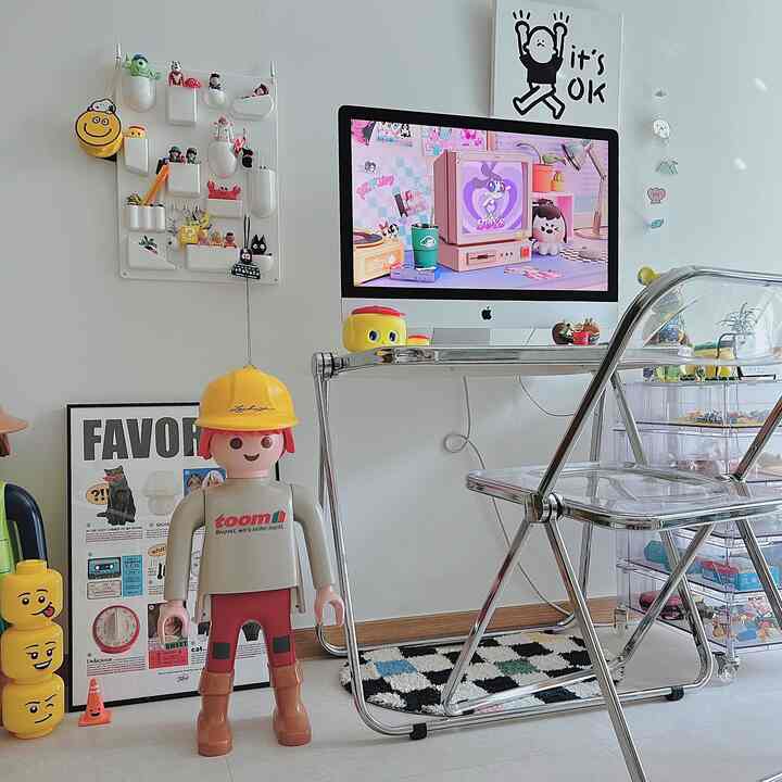 白い壁と床の小さなホームオフィス、透明なチェアとディズニーのフィギュア、かわいいキッドルートのデスクインテリアにアイマックが配置された空間